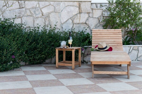 Eine Holzbank mit Hut und Flasche auf einer gefliesten Terrasse.