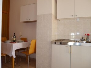 A kitchen with a stove, cabinets, and a dining table with chairs. - Dugi Rat Seaside Apartments - 2 Bedroom 6 (Dugi Rat)