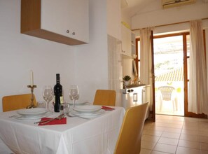 A dining area with a table set for four, a kitchen in the background, and a view through an open door. - Dugi Rat Seaside Apartments - 2 Bedroom 6 (Dugi Rat)