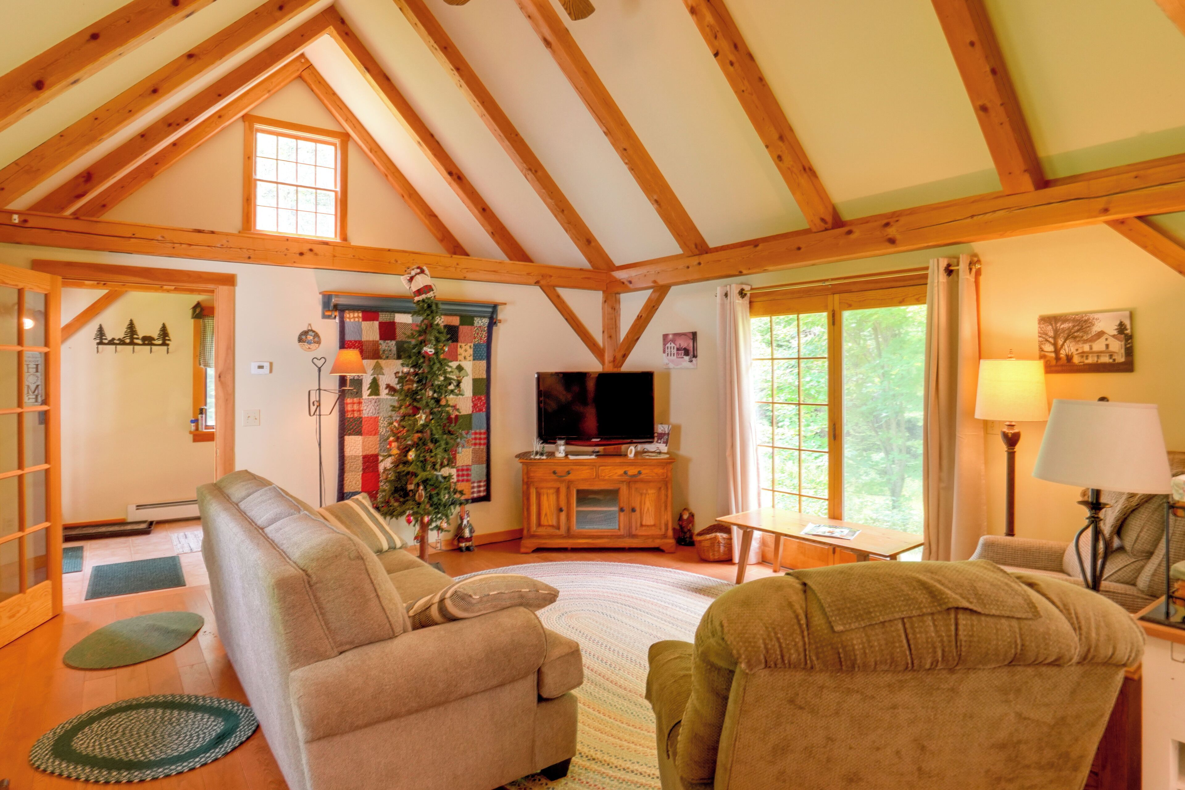 Una sala de estar acogedora con techo alto, vigas de madera, chimenea, televisor y un árbol de Navidad.