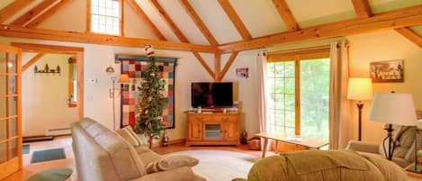 Ein gemütliches Wohnzimmer mit hoher Decke, Holzbalken, einem Kamin, einem Fernseher und einem Weihnachtsbaum.