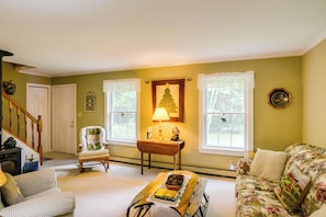 A living room with a sofa, a chair, a table with books, a lamp, and a Christmas tree decoration. - Deck & Wooded Views! Rural Windham Group Retreat (Windham)