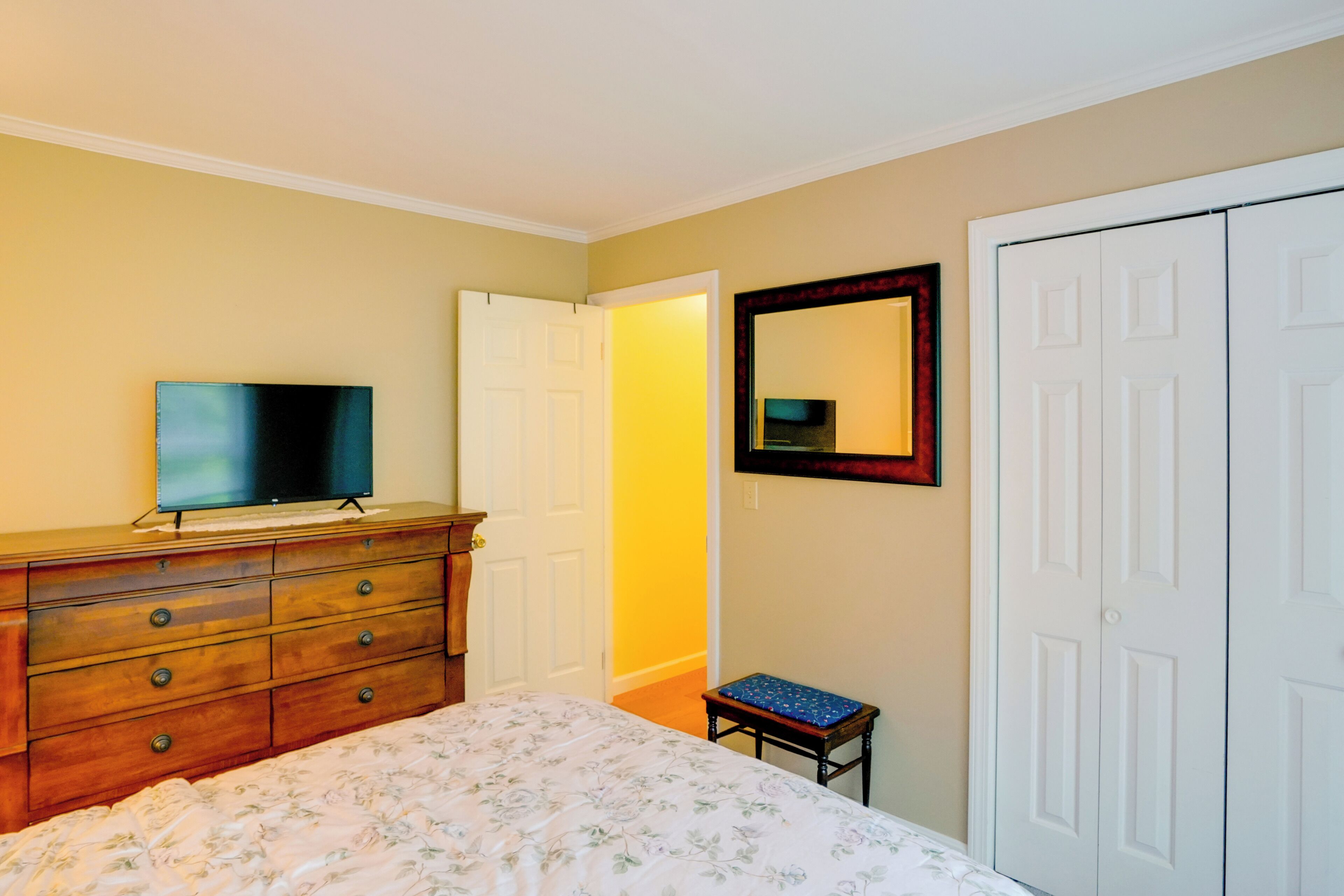 Ein Schlafzimmer mit Bett, Schminktisch, Fernseher, Kleiderschrank und einem kleinen Hocker.