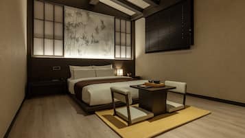 Quarto de hotel moderno com uma cama grande, mesas de cabeceira, uma pequena mesa com uma cadeira e vista para bambu através de um separador shoji.