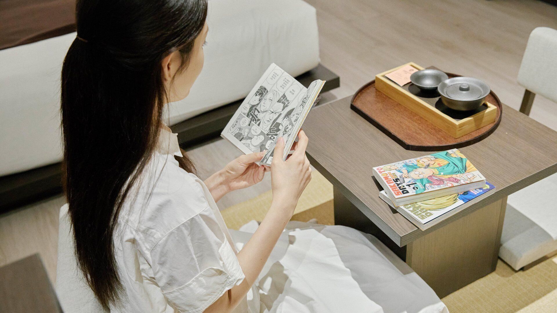 Una persona leyendo manga sobre una mesita con un cuenco y palillos a su lado.