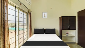 A hotel room with a bed, a wardrobe, a small shelf with a vase, and a window with curtains. - Super Collection O by OYO Nayagaon Vikas (Chikkamagaluru)