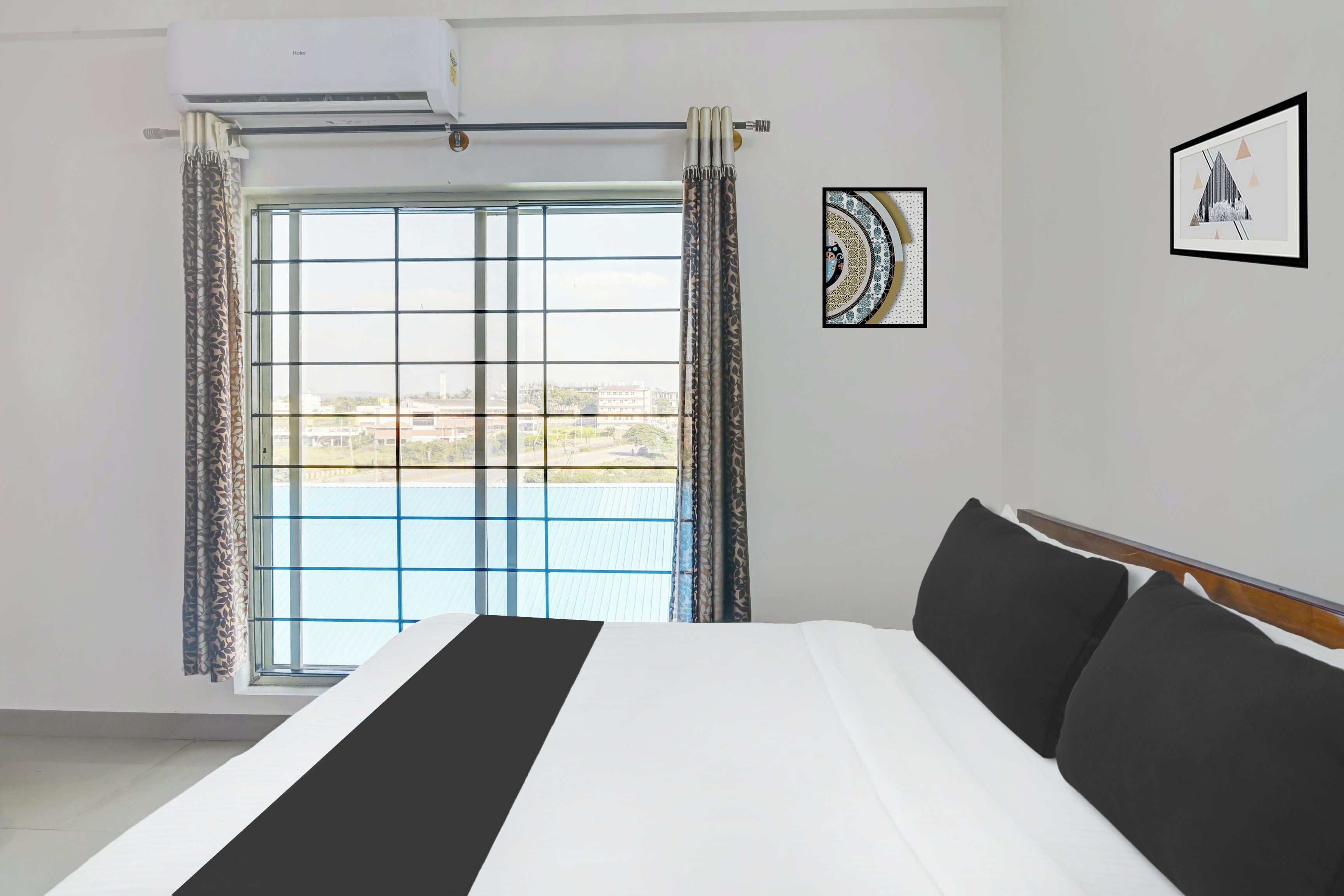 Quarto de hotel com uma cama grande, uma janela com cortinas e duas fotografias emolduradas na parede.