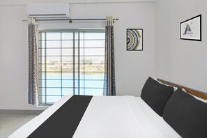 A hotel room with a large bed, a window with curtains, and two framed pictures on the wall. - Super Collection O by OYO Nayagaon Vikas (Chikkamagaluru)