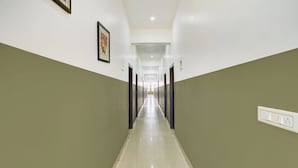 A long, narrow hallway with doors on both sides, a light switch on the right wall, and a framed picture on the left wall.