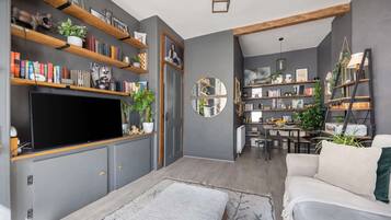 A modern living room with a flat-screen TV, bookshelves, a dining area, and a sofa.