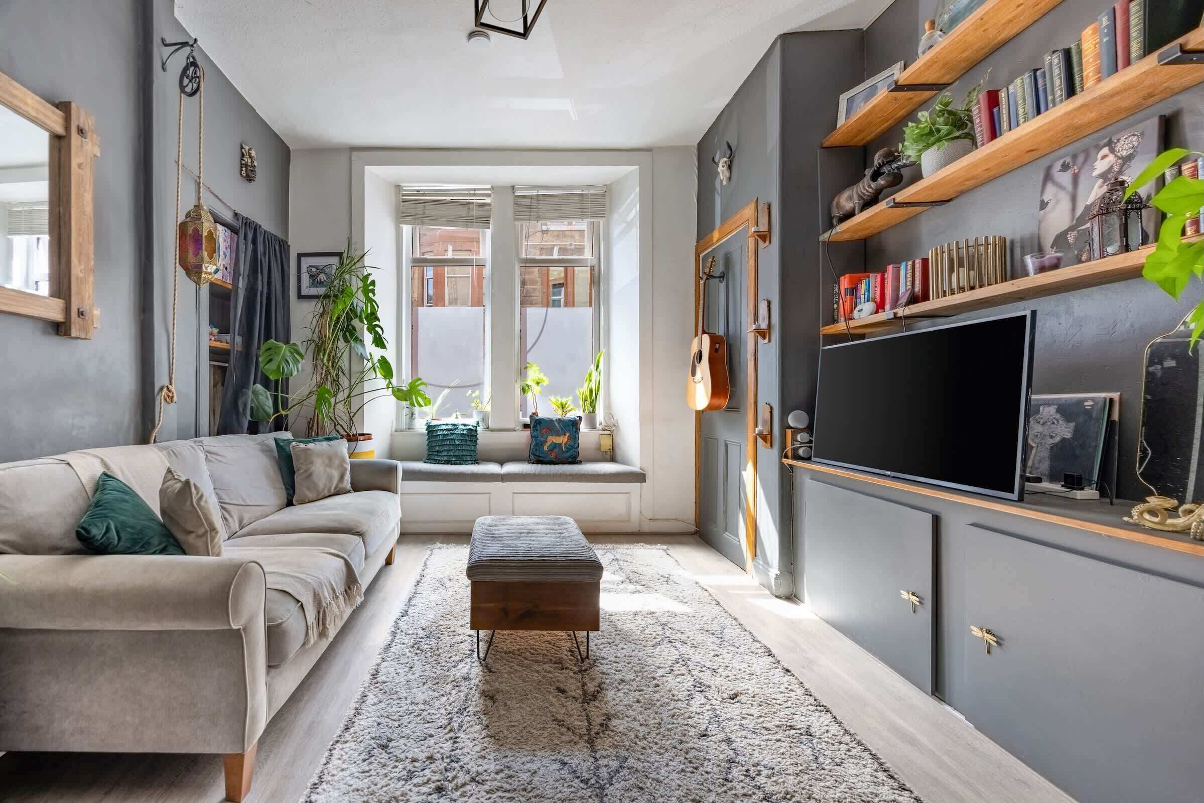 A living room with a sofa, a coffee table, a TV, and shelves with books and decorative items.