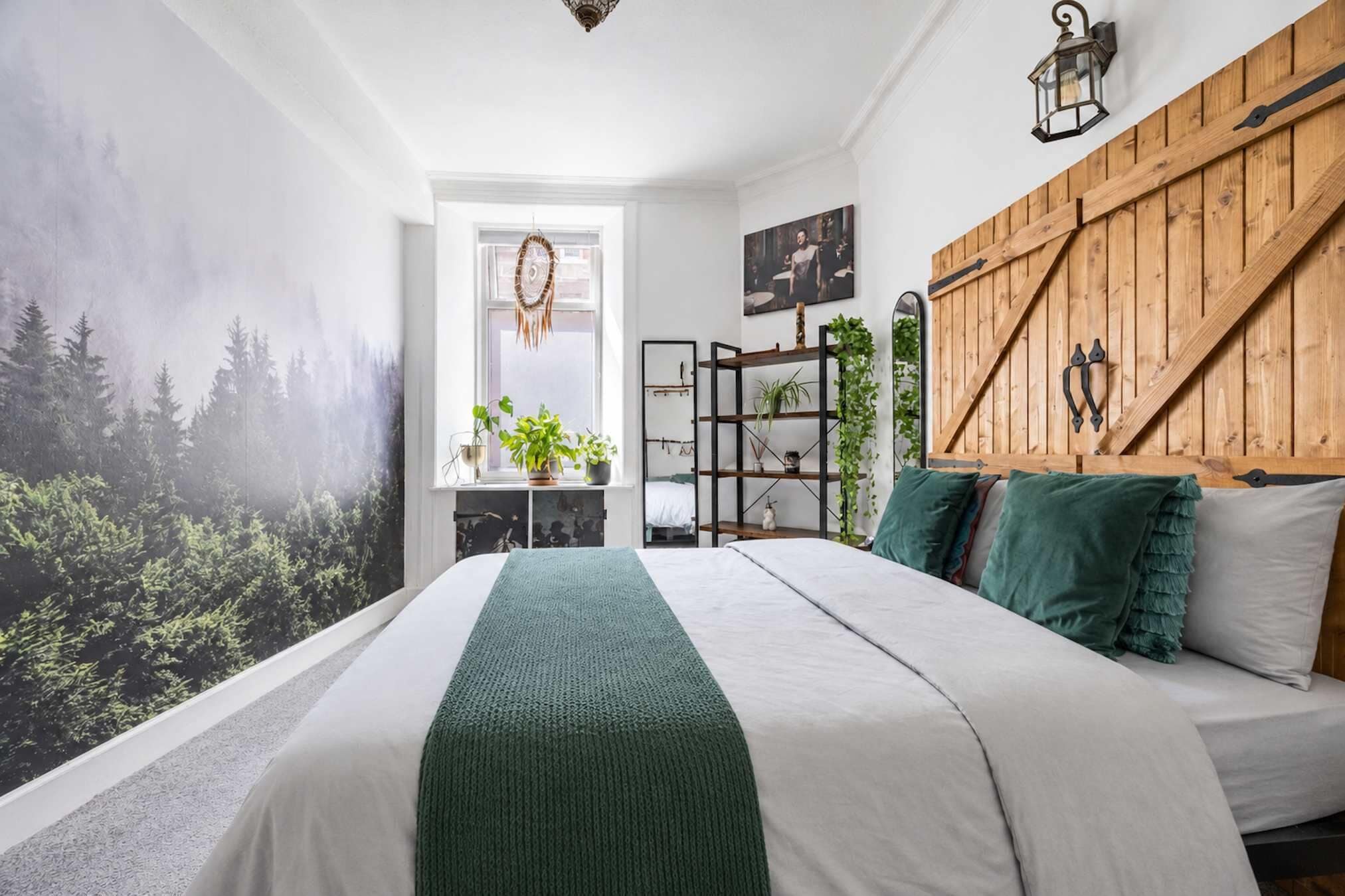 A bedroom with a bed, a wooden headboard, a wall-mounted shelf, and a window with a view of trees.