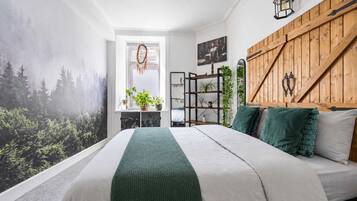 A bedroom with a bed, a wooden headboard, a wall-mounted shelf, and a window with a view of trees.