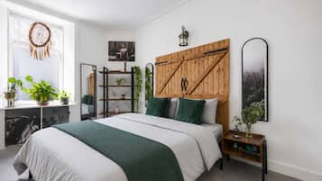 Une chambre à coucher avec un lit, une tête de lit en bois, une table de chevet, un miroir et une fenêtre ornée de plantes.