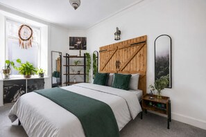 Un dormitorio con una cama, cabecera de madera, mesita de noche, espejo y ventana con plantas.