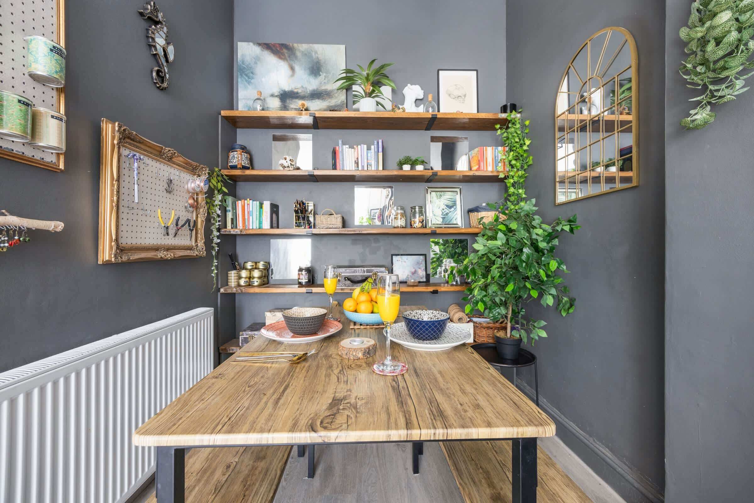 A dining area with a wooden table, shelves with books and decorative items, and a mirror on the wall.
