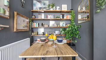 A dining area with a wooden table, shelves with books and decorative items, and a mirror on the wall.