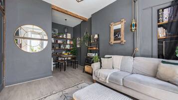 A modern living room with a grey sofa, a dining table, and a bookshelf.
