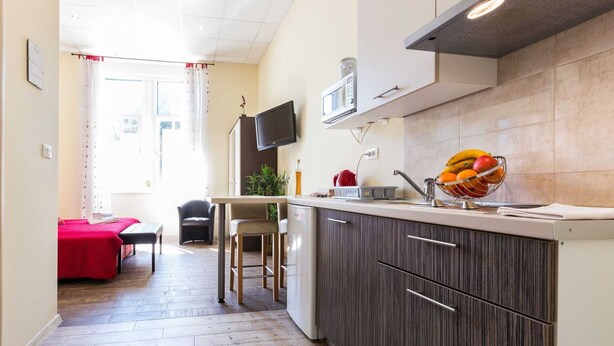 A modern kitchen with a built-in island, a dining area with a red table, and a living space with a TV. - Charming and Historic Old Town Apartments - Studio Apartment (Zadar)
