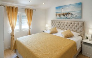 A hotel room with a large bed, a headboard, a painting of a lighthouse, and a window with curtains. - Lovely apartment in Drage with WiFi (Drage)