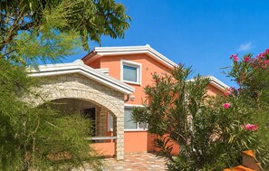 Uma casa com entrada em arco de pedra, um pátio com azulejos e um jardim com plantas floridas.