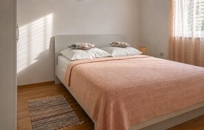Quarto com cama, almofadas, abajur e janela com cortinas.