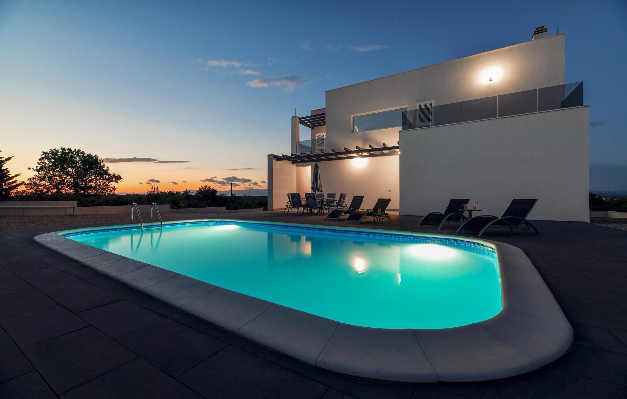 Una piscina con sillas de descanso y una pérgola, rodeada por un edificio moderno de techo plano.