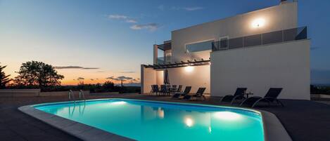 Una piscina con sillas de descanso y una pérgola, rodeada por un edificio moderno de techo plano.