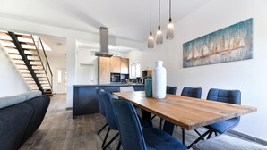 Ein moderner Essbereich mit Holztisch und blau gepolsterten Stühlen, im Hintergrund eine Küche und eine Treppe, die zu einer anderen Ebene führt.