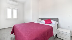 Ein Schlafzimmer mit einem Bett, einem Nachttisch, einem Fenster und einer Klimaanlage.