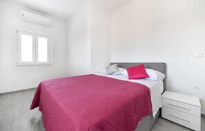 Ein Schlafzimmer mit einem Bett, einem Nachttisch, einem Fenster und einer Klimaanlage.