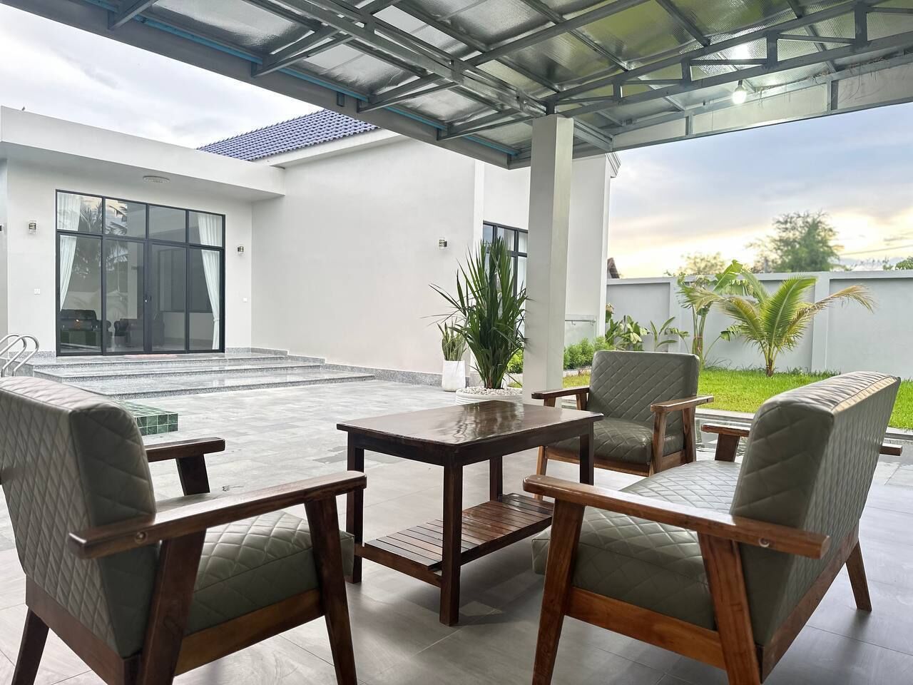 Une terrasse extérieure avec une table et des chaises, un plafond en verre et une vue sur un bâtiment et de la verdure.