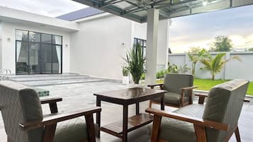 Um pátio externo com mesa e cadeiras, teto de vidro e vista para um edifício e vegetação.
