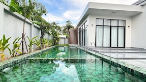 A swimming pool with clear water, surrounded by plants and a modern building with large windows.