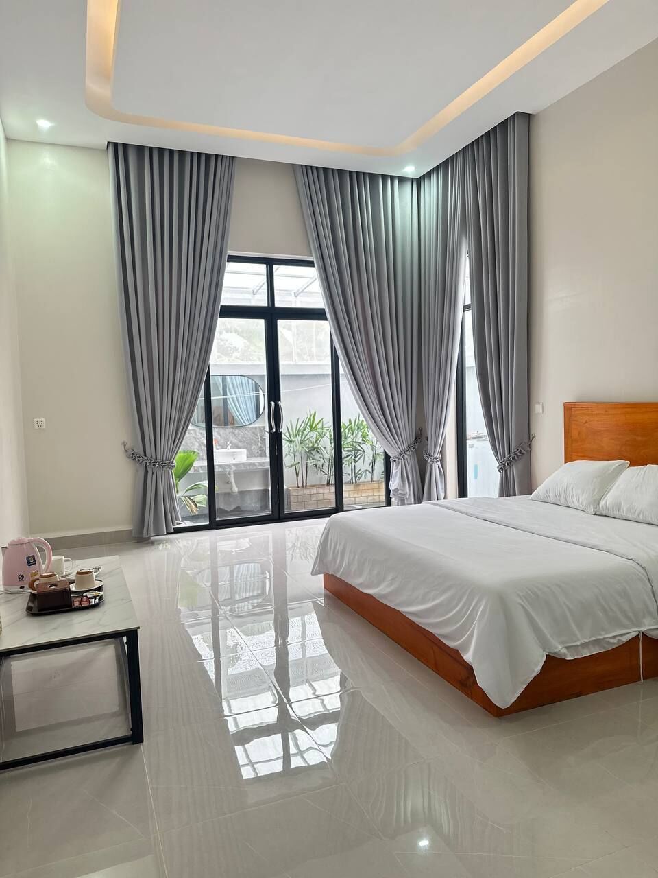 A modern bedroom with a large bed, a glass table, and curtains.