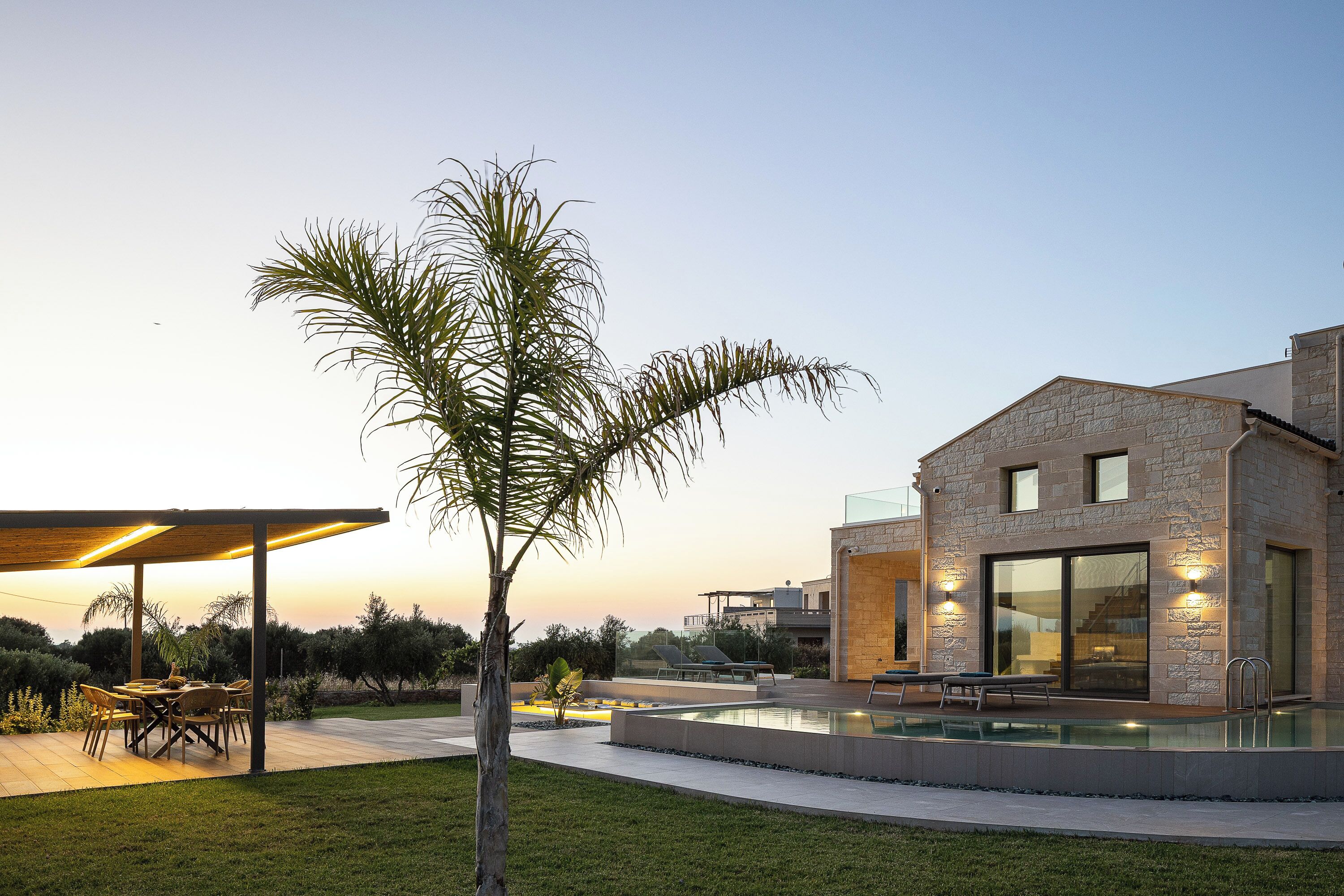 A modern house with a stone facade, a swimming pool, and a patio area with outdoor furniture.