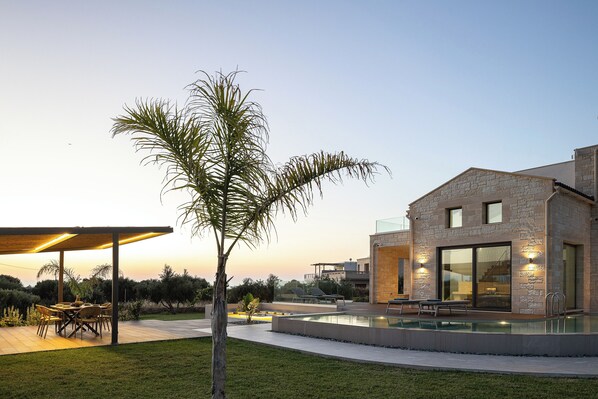 A modern house with a stone facade, a swimming pool, and a patio area with outdoor furniture.