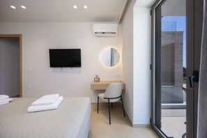 A modern hotel room with a flat-screen TV, a round mirror, a wooden desk, and a chair.