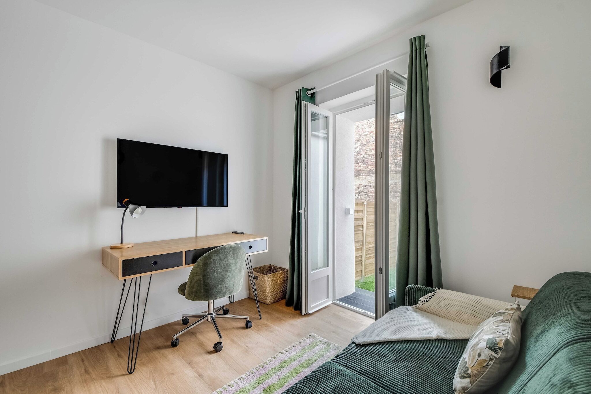 A bedroom with a desk, chair, bed, and a TV mounted on the wall.
