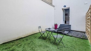 Un petit espace extérieur avec du gazon synthétique, une table, deux chaises et une plante en pot.