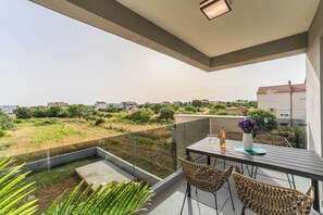 Ein Balkon mit Tisch, Stühlen und einer Weinflasche, mit Blick auf eine Wohngegend mit Grünflächen und Häusern.