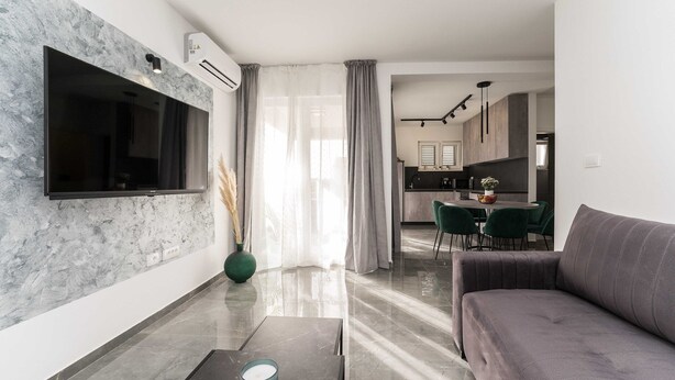 A modern living room with a flat-screen TV, a sofa, a coffee table, and a dining area with green chairs. - Luxury D Apartments - Luxury Two Bedroom Apartment With Terrace A2 (Bibinje)