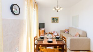 Un comedor con una mesa de madera para dos personas, un sofá, un televisor y un cuadro en la pared.