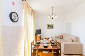 Ein Essbereich mit einem Holztisch, gedeckt für zwei Personen, einer Couch, einem Fernseher und einem Gemälde an der Wand.