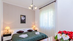 Habitación de hotel con cama, dos lámparas de noche, mesita de noche, un jarrón con flores y una ventana con cortinas.