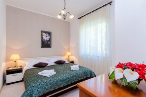 Ein Hotelzimmer mit einem Bett, zwei Nachttischlampen, einem Nachttisch, einer Ablage neben dem Bett, einer Vase mit Blumen und einem Fenster mit Vorhängen.