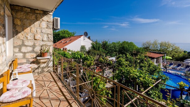 Un balcón con pared de piedra, una piscina y vista al mar.