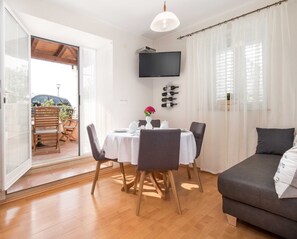 Ein helles Zimmer mit Esstisch für zwei Personen, einer Couch und einem an der Wand befestigten Fernseher.
