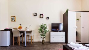 A hotel room with a bed, a desk with a chair, a television, a wardrobe, and a small plant. - Charming and Historic Old Town Apartments - Double Room (Zadar)