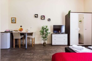 Ein Hotelzimmer mit Bett, Schreibtisch mit Stuhl, Fernseher, Kleiderschrank und einer kleinen Pflanze.